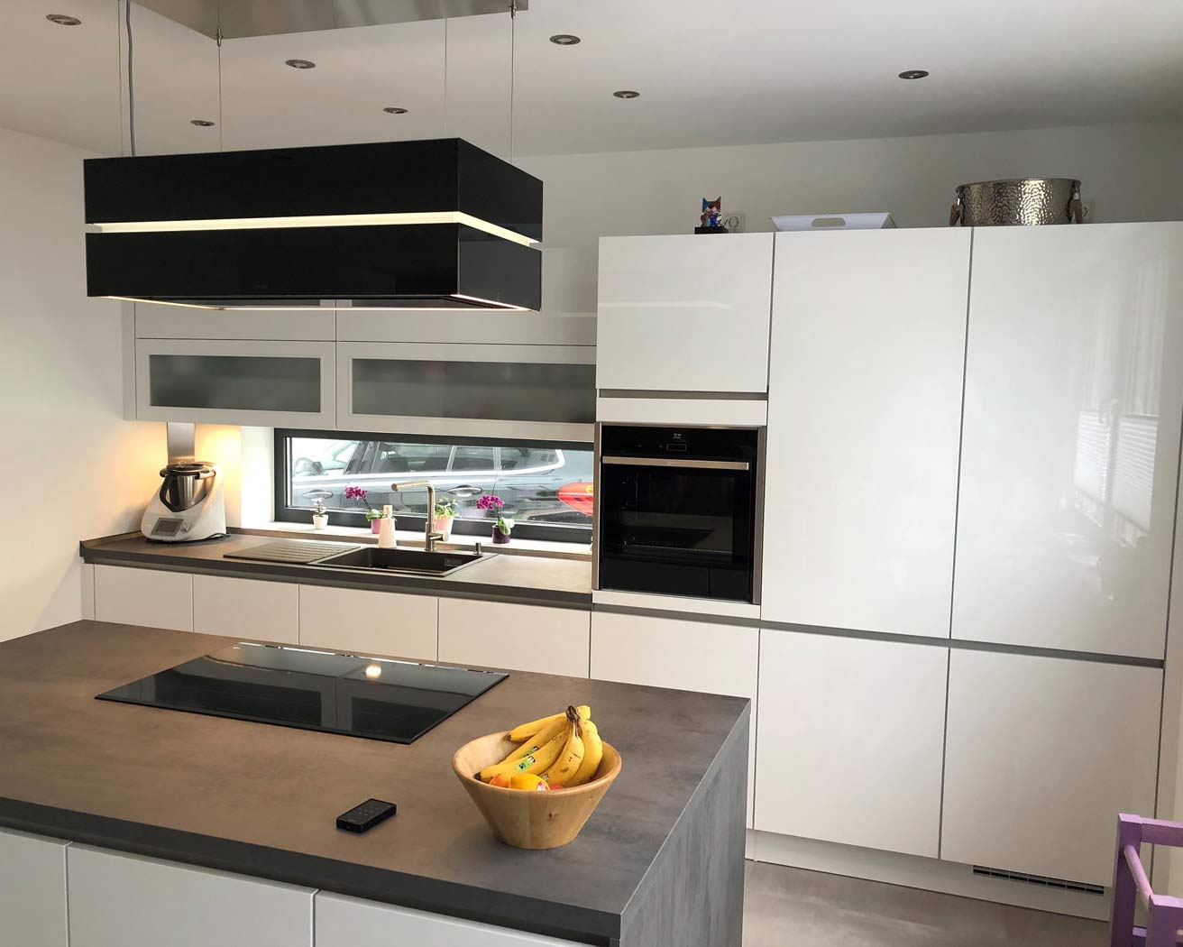 Die weiße Hochglanz-Küche mit Kochinsel punktet mit modernen grifflosen Fronten und einer Arbeitsplatte in Beton-Optik
